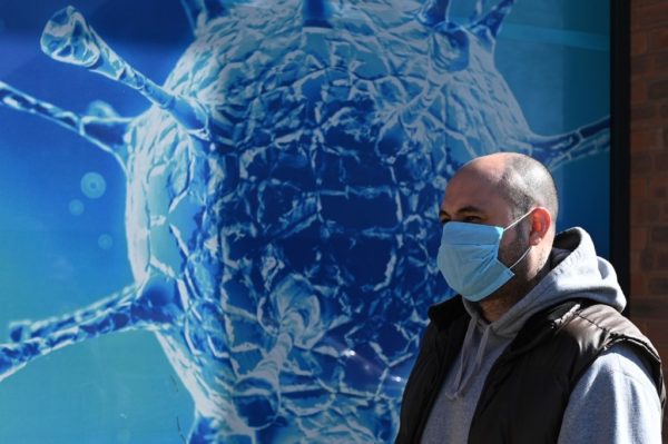 A man wearing a mask walks past the Regional Science Centre in Oldham, Lancashire on March 26, 2020, during a country-wide lockdown to slow the spread of the novel coronavirus COVID-19. (Photo by Oli SCARFF / AFP)